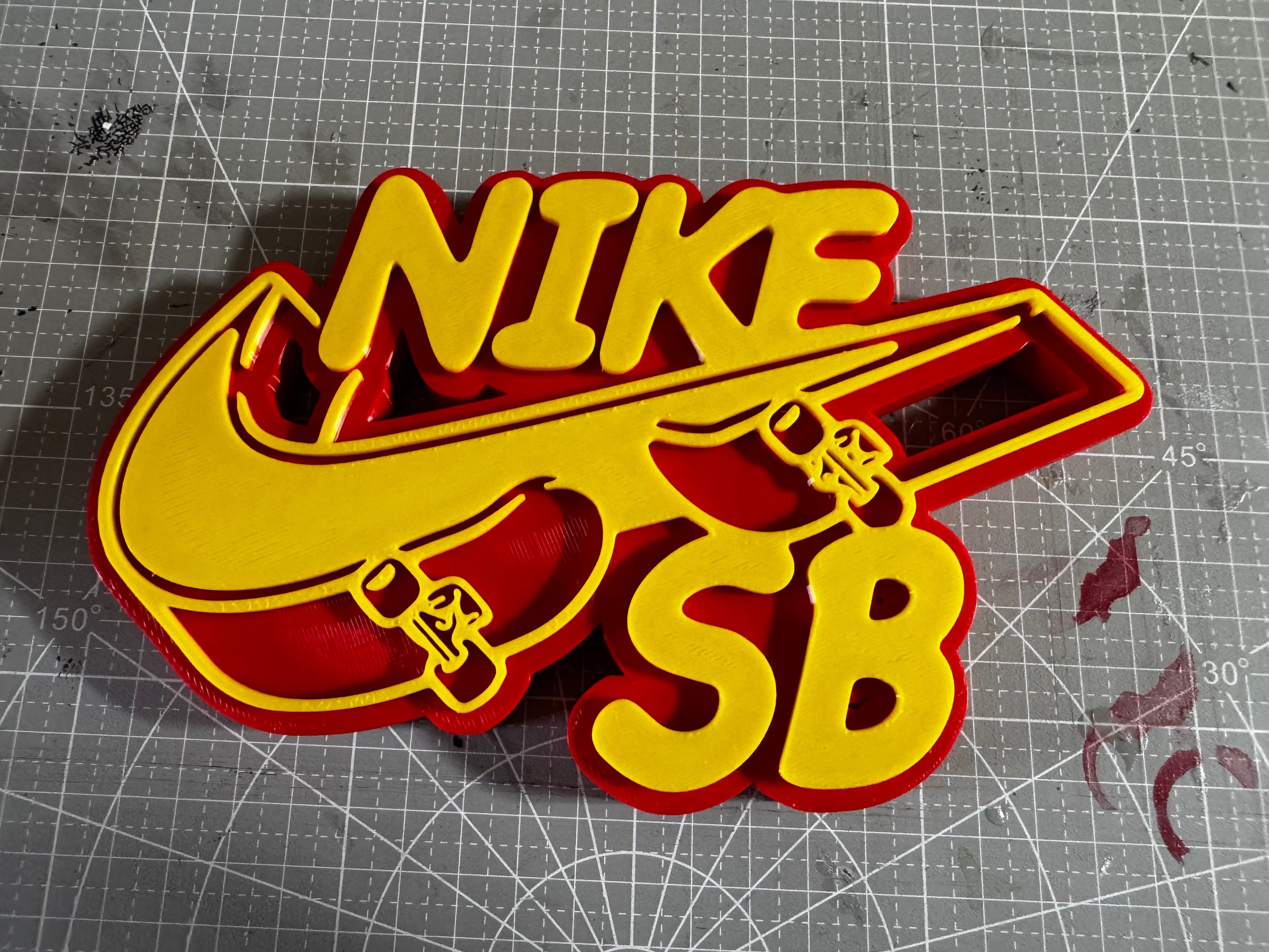 A yellow and red plastic cookie cutter shaped like a stylized Nike SB logo, displayed on a gray gridded cutting mat.